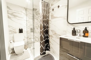 Ein modernes Badezimmer mit Duschkabine aus Glas, Toilette, Waschbecken mit Seifenspendern und einem Spiegel.