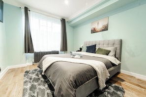 Ein Schlafzimmer mit einem Bett, einem Fenster mit Vorhängen, einem Bild an der Wand und einem flauschigen Teppich.