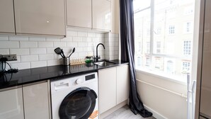 A compact kitchen with a washing machine, a sink, and a window with a view of buildings. - Luxury 2-Bedroom Apartment on Iconic Baker Street | Central London (London)