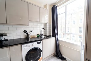 Eine kleine Küche mit Waschmaschine, Spüle und einem Fenster mit Blick auf Gebäude.