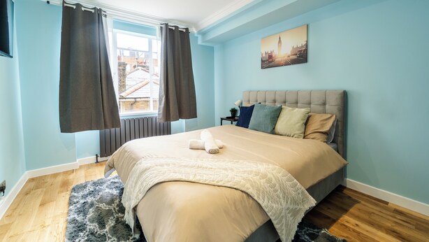 A bedroom with a bed, curtains, a window, and a painting on the wall. - Luxury 2-Bedroom Apartment on Iconic Baker Street | Central London (London)