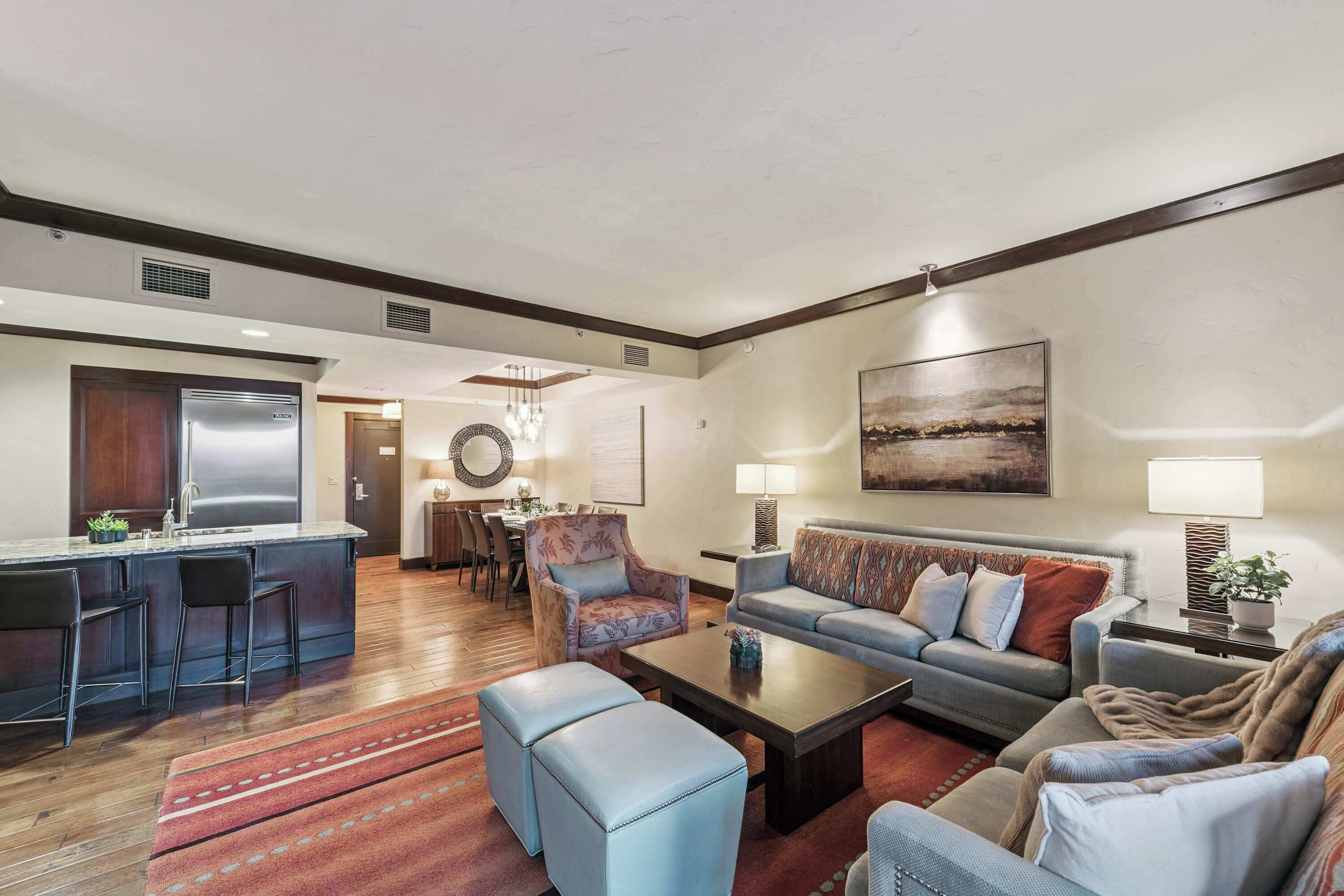 A modern living room with a sofa, ottoman, coffee table, and a dining area with chairs and a chandelier.