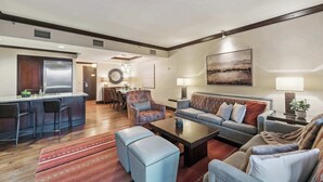 En moderne stue med sofa, skammel, sofabord og et spiseområde med stole og en lysekrone.