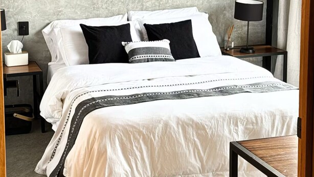 A bedroom with a wooden headboard, a bed with white and black bedding, a bedside table with a lamp, and a nightstand with a tissue box. - Upscale 2BR/2BA Apartment with Incredible Mountain Views (Oaxaca de Juárez)