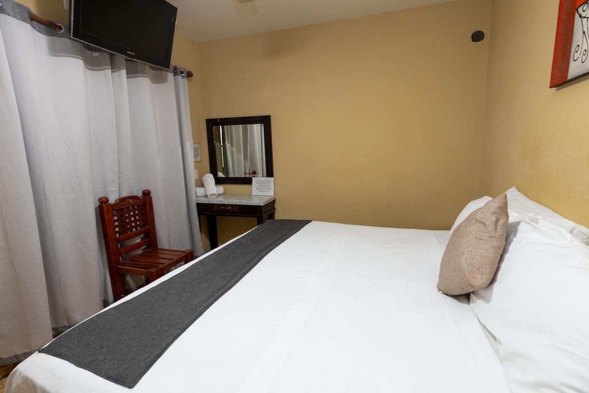 Ein Hotelzimmer mit einem Bett, einem Sessel, einem Schreibtisch, einem Spiegel und einem Fernseher.