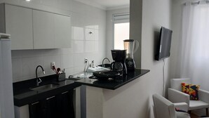 A modern kitchen with white cabinets, a black countertop, a coffee maker, a blender, and a TV mounted on the wall. - Apartment with 2 bedrooms, swimming pool and private parking. Pets allowed. (Londrina)