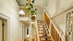 Una escalera con peldaños de madera y barandillas blancas, que conduce a un rellano en el segundo piso con una planta colgante.