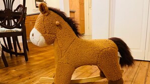 Un caballo balancín en una habitación con piso y silla de madera.