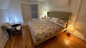 Un dormitorio con cama, lámparas de noche, una silla y una ventana con persianas.