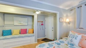 Une chambre à coucher avec un lit, un banc doté de coussins, une porte et un luminaire fixé au mur.
