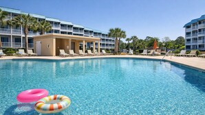 Une piscine d’un bleu éclatant, avec des chaises longues, et un bâtiment doté de balcons en arrière-plan.