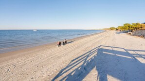 Une plage avec un ciel dégagé, une mer calme et quelques personnes qui pêchent.