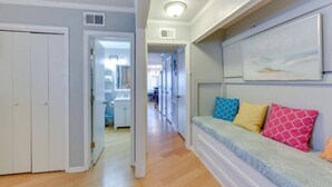 Un couloir avec un plancher en bois, une porte blanche et un banc agrémenté de coussins colorés.