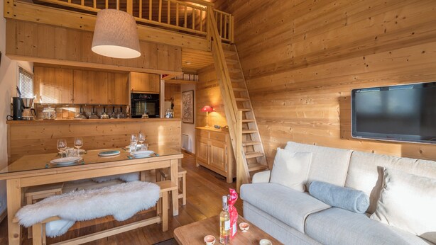 Een knus houten blokhut interieur met een eethoek, bank en een aan de muur bevestigde televisie.