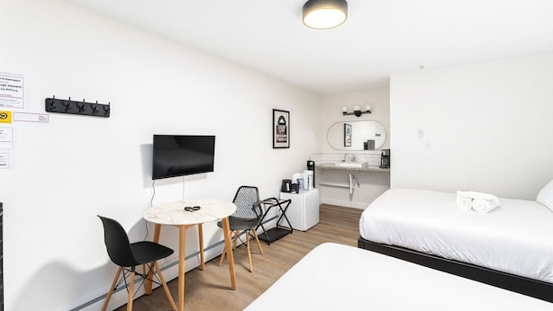 Une chambre d’hôtel comprenant un lit, un bureau avec une chaise, une télévision, une petite kitchenette et une salle de bain.
