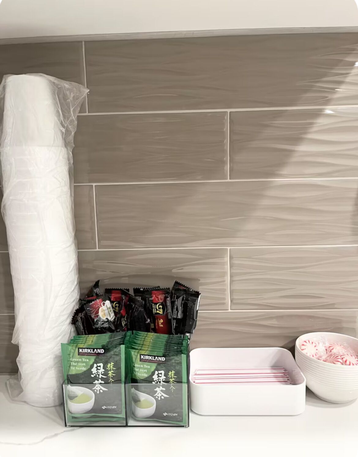 A kitchen counter with a white towel, two boxes of Kirkland Green Tea, a white tray, and a bowl of pink candy.