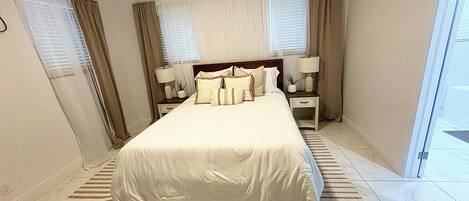 A hotel room with a large bed, two bedside tables with lamps, a window with curtains, and a striped rug.