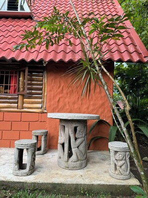 A traditional house with a red tiled roof, a wooden window with a red curtain, and a stone table with stools in front. - Rustic Chalet Cabin for 6•Private Pool-Gym Access (La Fortuna)
