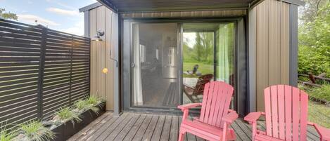 Een overdekt buitengebied met een schuifdeur naar een keuken, twee roze Adirondack stoelen en een houten terras.