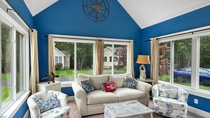 Una sala de estar con una pared azul de acento, un sofá color crema, sillones estampados, una mesa de centro y ventanas amplias con cortinas.