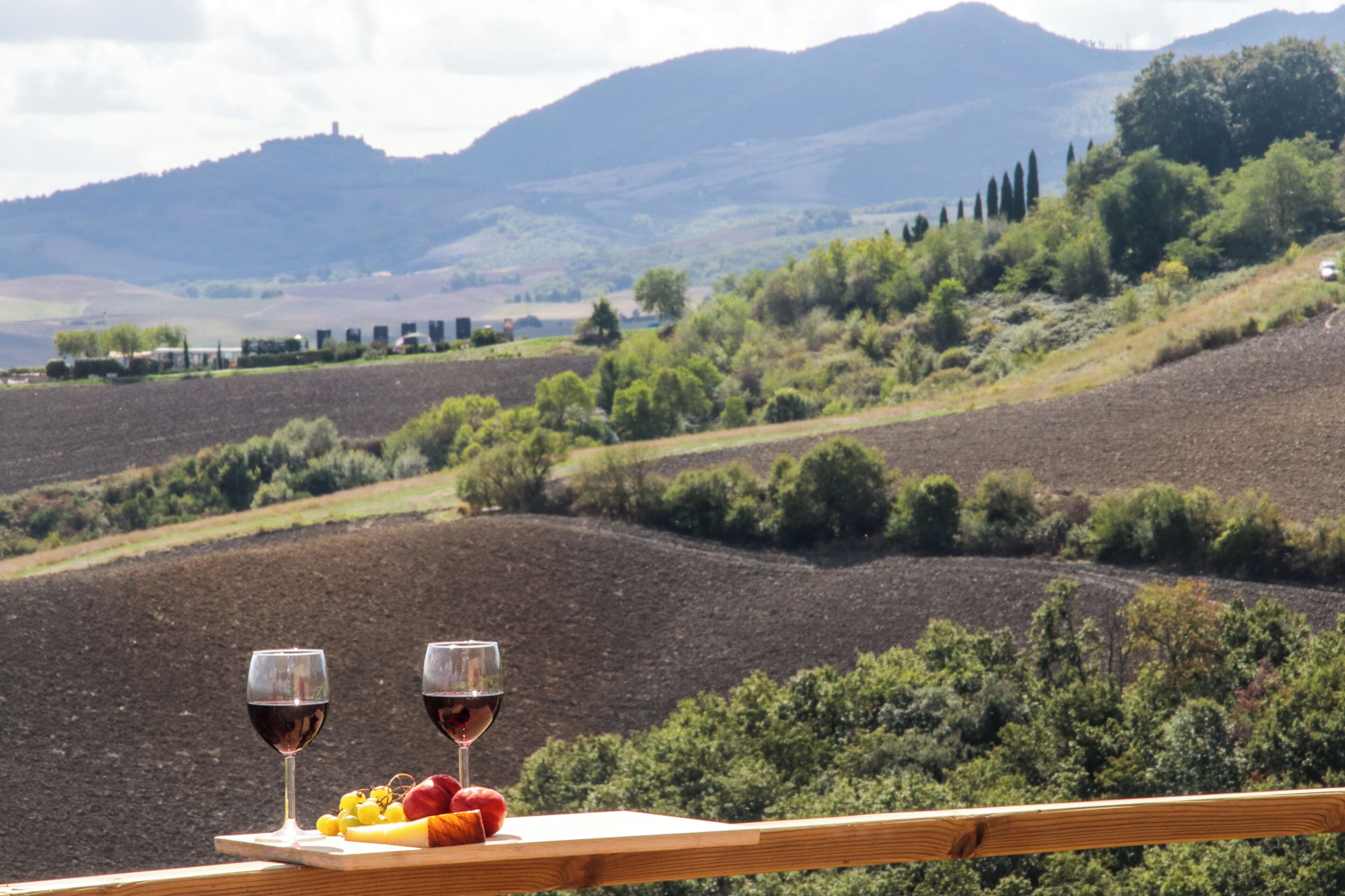 A scenic view from a balcony with two glasses of red wine and a plate of fruit.