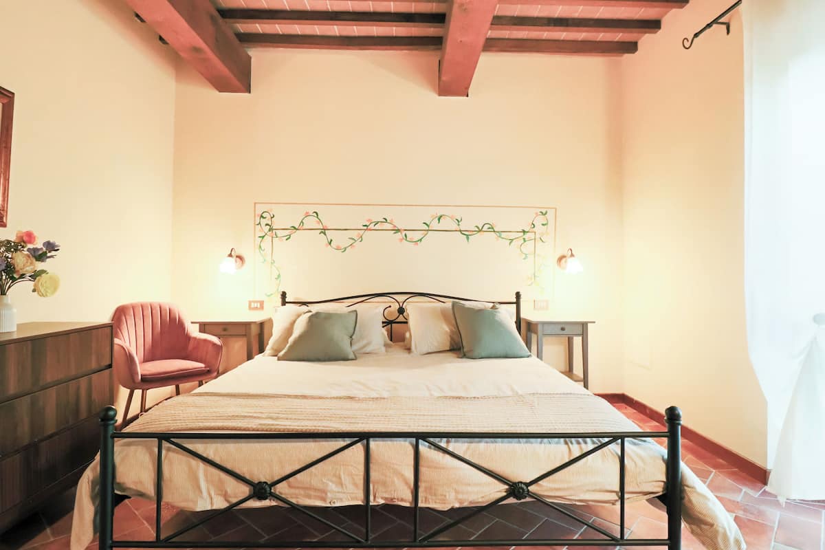 A bedroom with a bed, a chair, a nightstand, and a wall-mounted light fixture.
