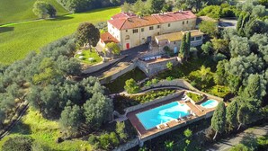 Vue aérienne d’une villa dotée d’une piscine, entourée d’une végétation luxuriante et de vignobles.