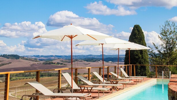 Un espace aménagé au bord de la piscine, avec des chaises longues et des parasols, offrant une vue sur un paysage pittoresque.