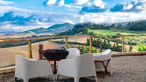 Une terrasse avec des chaises et une table en plastique blanc, offrant une vue panoramique sur un paysage vallonné et boisé.
