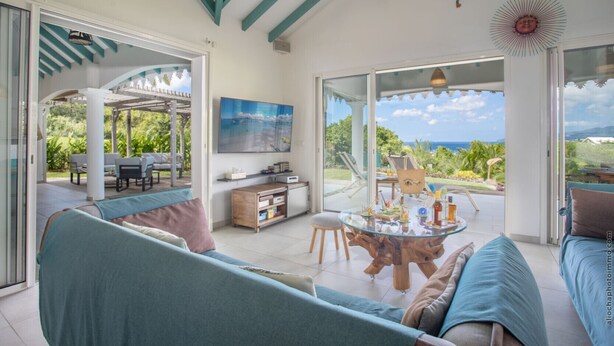 A spacious living area with a large glass door leading to a patio, a wooden coffee table, and a comfortable seating arrangement. - Coralyne (Les Trois-Ilets)