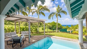 A pool area with a covered seating area, palm trees, and a view of the ocean. - Coralyne (Les Trois-Ilets)