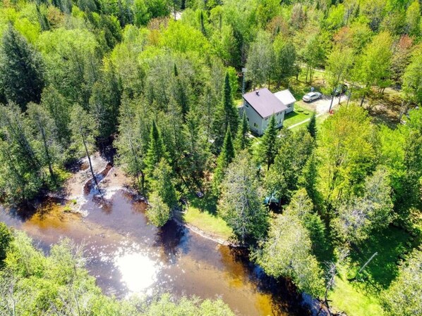 An aerial view of a house surrounded by dense forest, with a small stream nearby.