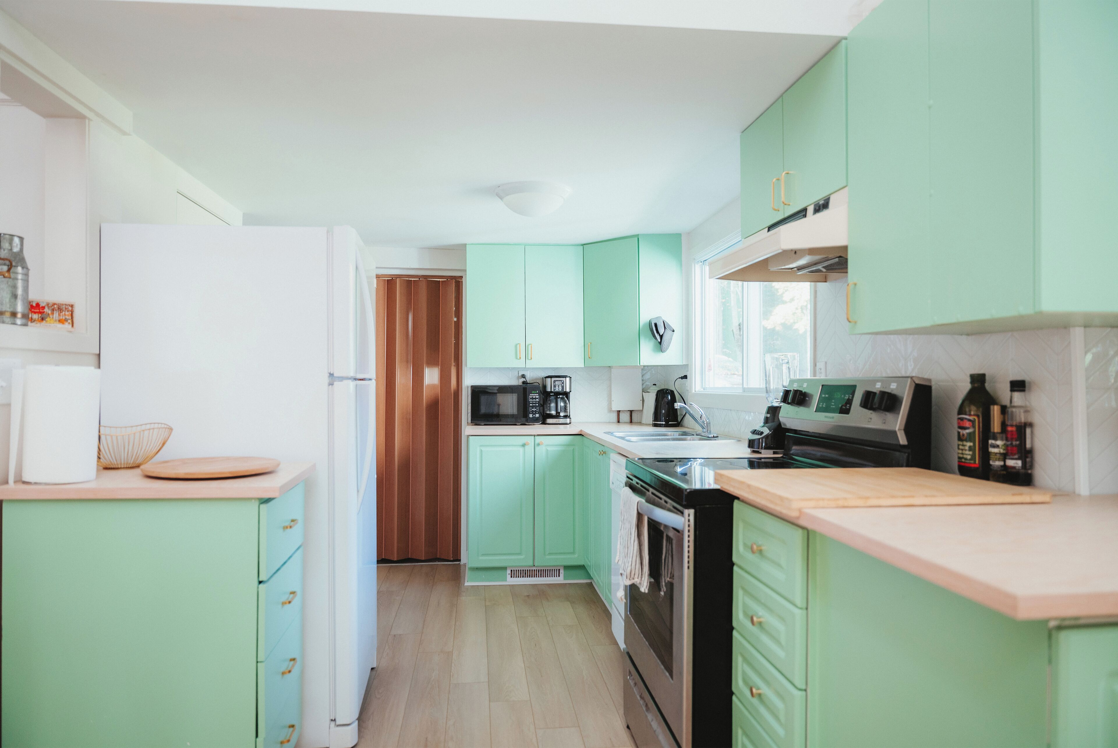 A compact kitchen with green cabinets, a microwave, a coffee maker, and a stove.
