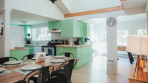 A spacious kitchen with green cabinets, a dining area with a wooden table and chairs, and a loft bedroom with a wooden ceiling.
