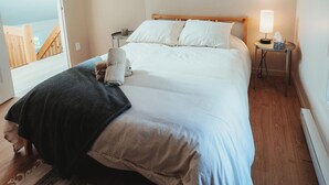 A bedroom with a bed, a bedside table with a lamp, a window with a view, and a door leading to a balcony.