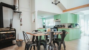 A modern kitchen with green cabinets, a dining table with chairs, and a wood-burning stove.