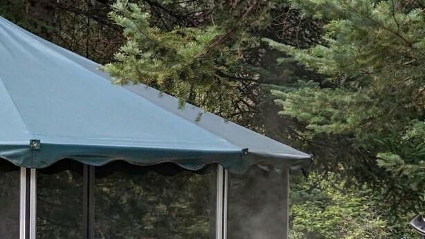 A person relaxing in a hot tub under a canopy, surrounded by trees.