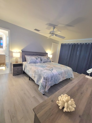 Ein Schlafzimmer mit einem Bett, Nachttischen, einem Deckenventilator und einem Holztisch mit einem dekorativen Gegenstand.