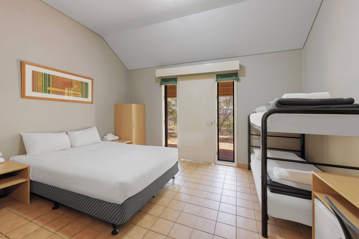 A bedroom with a bed, a bunk bed, a nightstand, a wardrobe, and a door leading to an outdoor area.