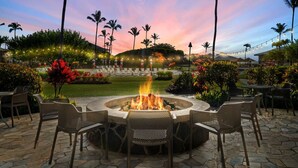 A circular outdoor seating area with a fire pit, surrounded by stone tiles and wicker chairs. - Just Listed! Oceanfront Paradise Views and Luxury (Lihue)