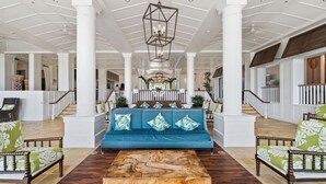 A spacious lobby with a central blue sofa, wooden coffee table, and wicker chairs with green cushions. - Just Listed! Oceanfront Paradise Views and Luxury (Lihue)