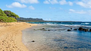 A beach with clear blue water, sandy shore, and a forested area in the background. - Just Listed! Oceanfront Paradise Views and Luxury (Lihue)