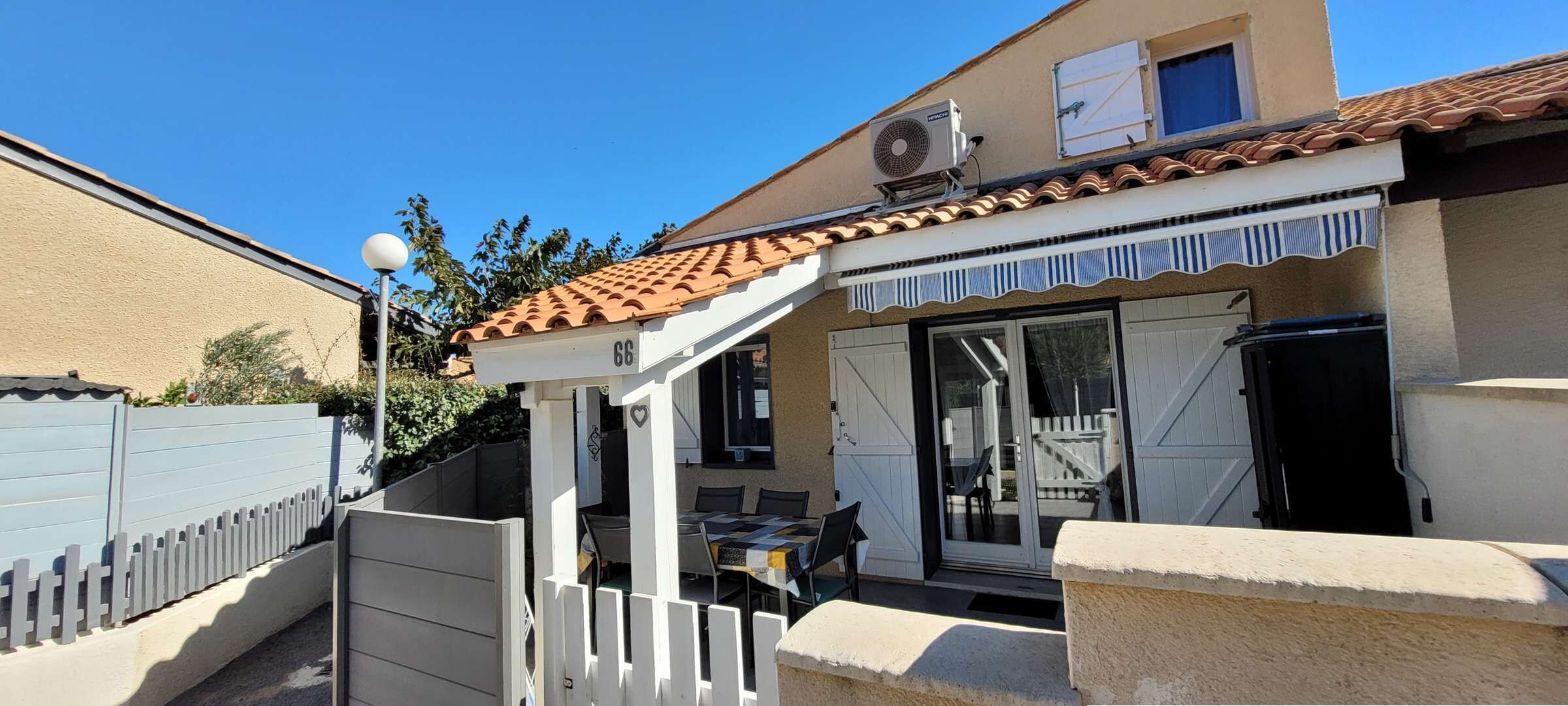 Ein Wohnhaus mit Terrasse, einer Schiebetür als Eingang und einer kleinen Sitzgelegenheit im Freien.