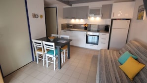 A compact kitchen with white cabinets, a dining table with chairs, and a built-in oven. - Lovely corner house,well equipped for 5 people, Airco upstairs, in a secured residence LE VILLAGE... (PORTIRAGNES)