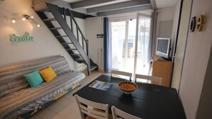 A living room with a sofa, a dining table with chairs, a television, and a staircase. - Lovely corner house,well equipped for 5 people, Airco upstairs, in a secured residence LE VILLAGE... (PORTIRAGNES)
