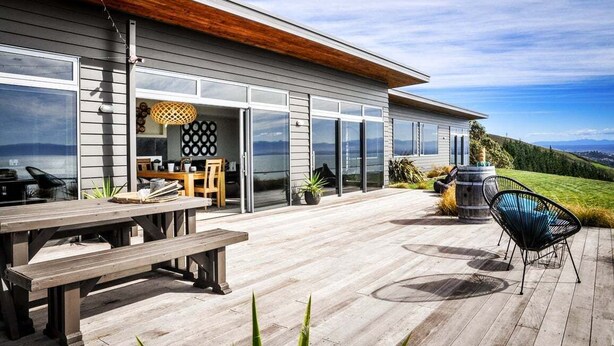 Een modern huis met een terras, een houten bank en een zwarte stoel.