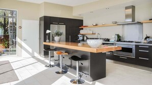 Een moderne keuken met een centraal eiland, zwarte kasten, roestvrijstalen apparatuur en een groot raam dat voor natuurlijk licht zorgt.