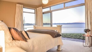 Een slaapkamer met een groot bed, uitzicht op zee en een kleine tafel met een vaas.