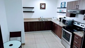 Cocina compacta con armarios de madera oscura, encimera de granito, microondas, estufa y una pequeña mesa de comedor.