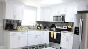 Una cucina moderna con mobili bianchi, un frigorifero in acciaio inox, un forno a microonde e una macchina per il caffè.